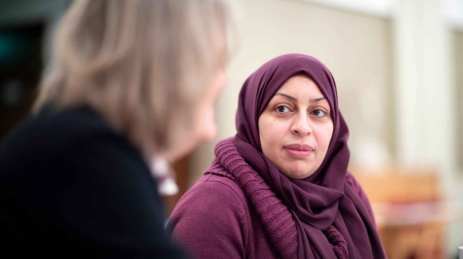 Dame i hijab lytter til dame uten hijab, som ses uskarpt i forgrunnen i bildet.